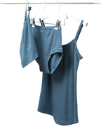 A strappy steel blue vest and pants set hanging on a rod with a drawstring bag.